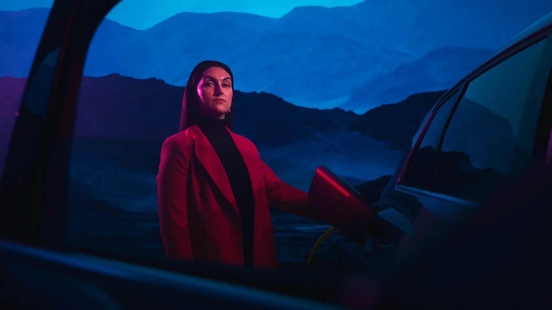 Businessfrau beim Laden eines E-Autos vor blauem Nachthimmel