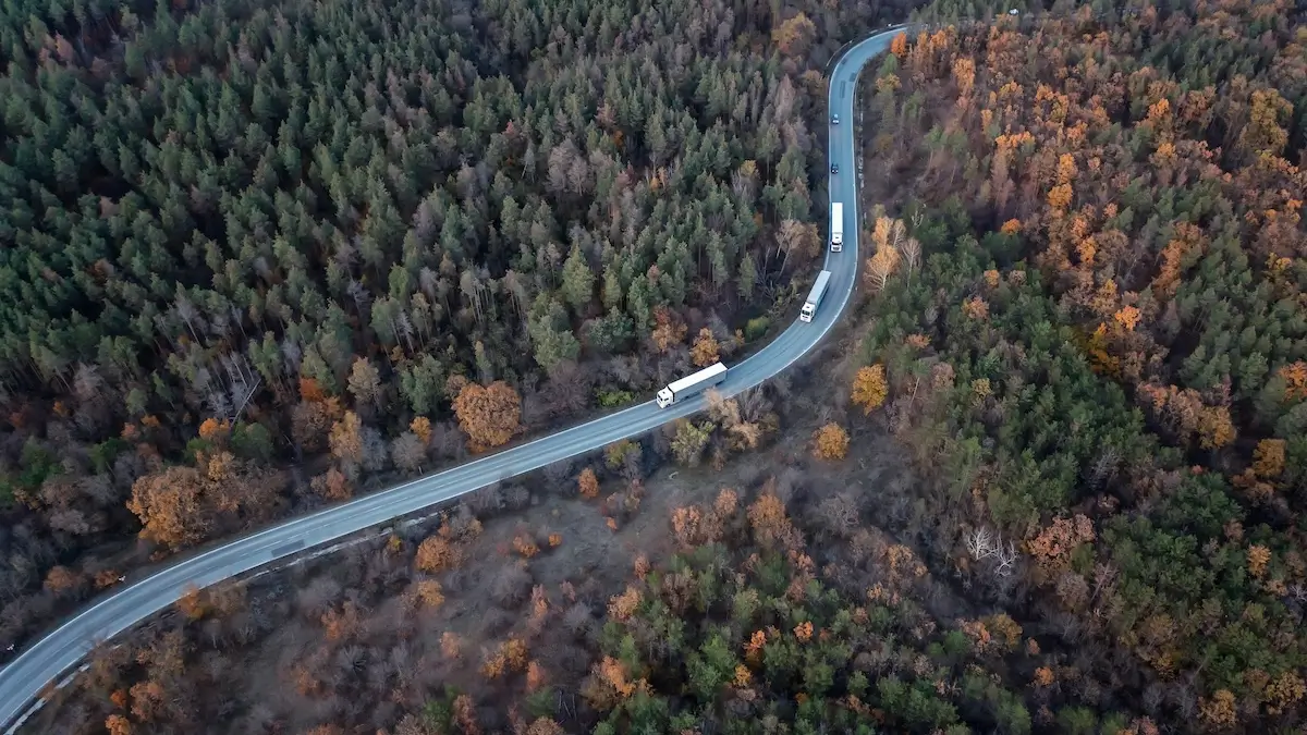 bird-view-of-heavy-duty-trucks-driving-through-autumn-forest-on-a-curved-road