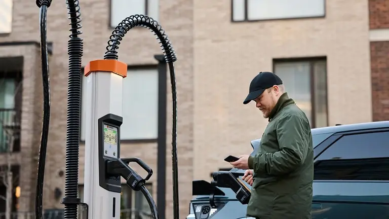 Man wearing a cap looks at his phone in front of HPC charger in residential area