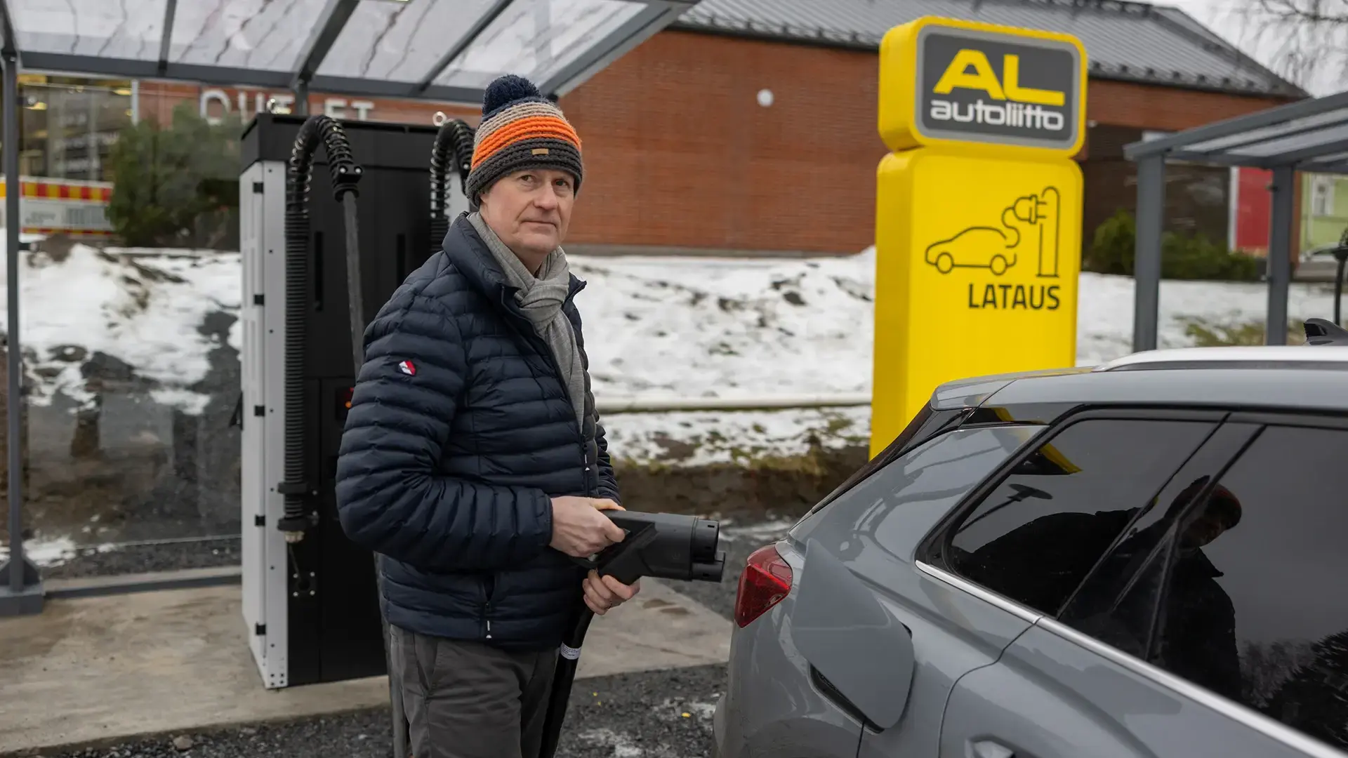 Man standing beside EV with fast charging connector outside store