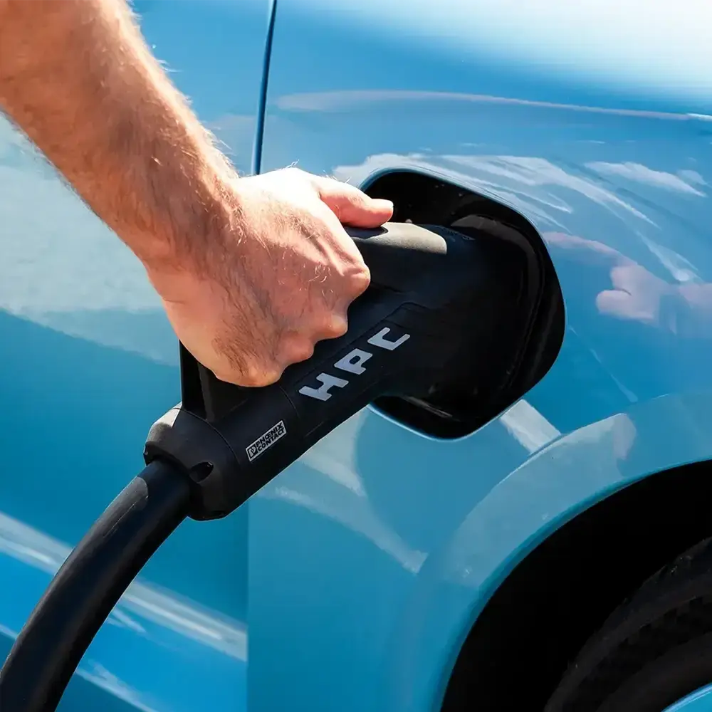 Blue EV with man holding HPC charging station connector
