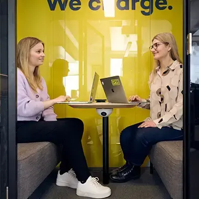 Två kvinnor i ett mötesrum med gul vägg