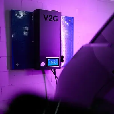 Vehicle-to-grid-laddare bakom elbil i garage med lila belysning