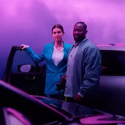 Frau und Mann laden E-Auto mit Windrädern und lila Hintergrund