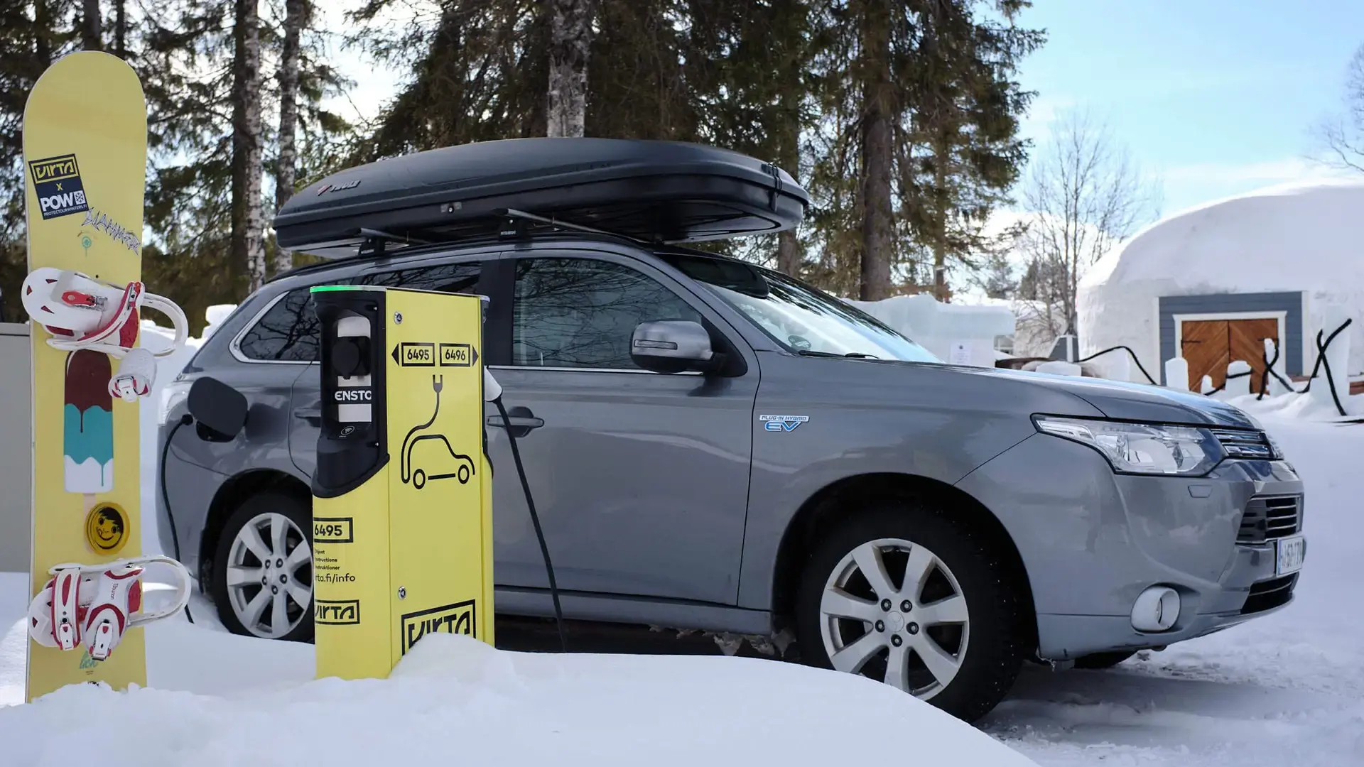 Grey car charging at Virta charger next to a snowboard in snow