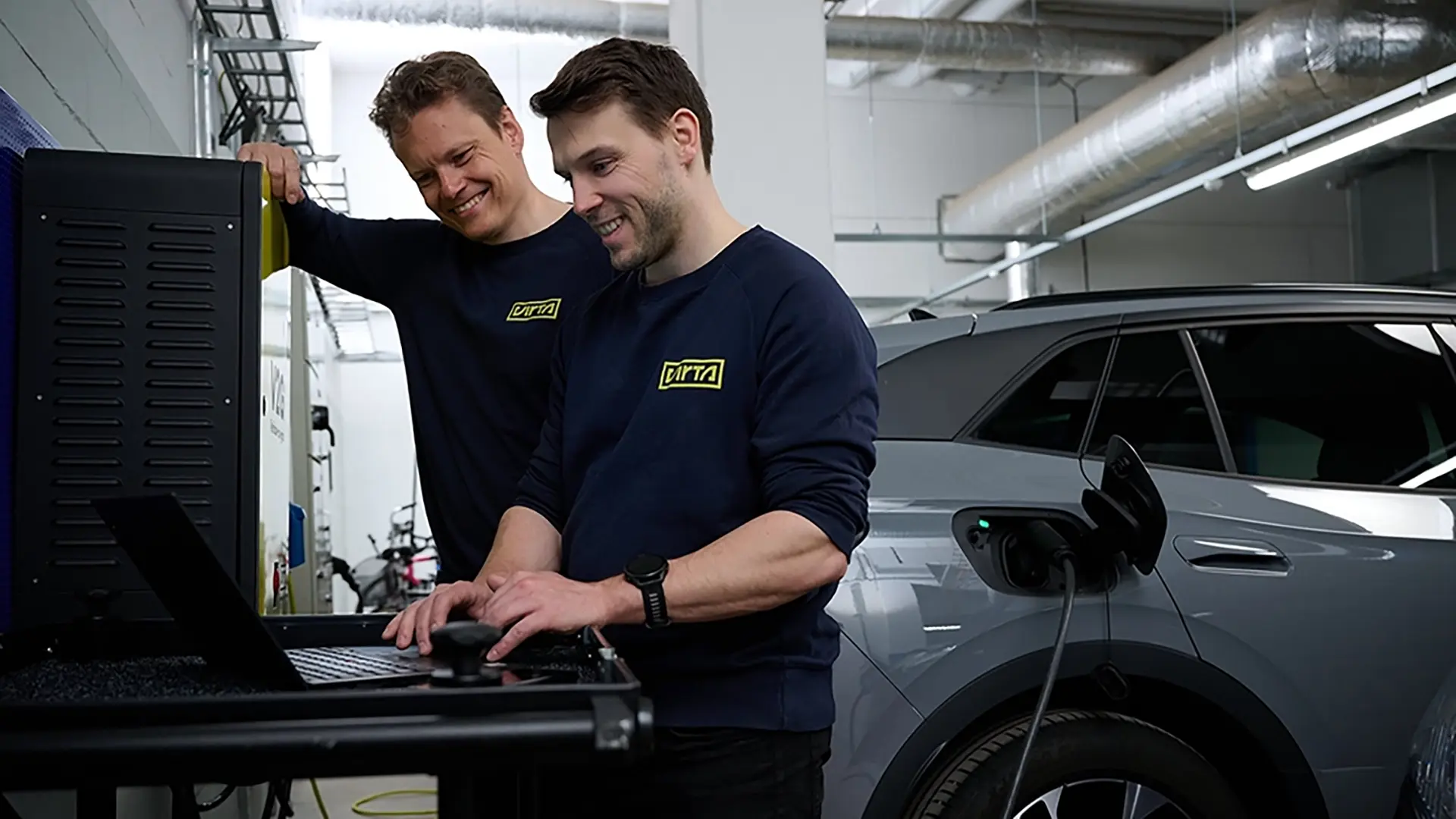 Two men working next to a charging car in a garage