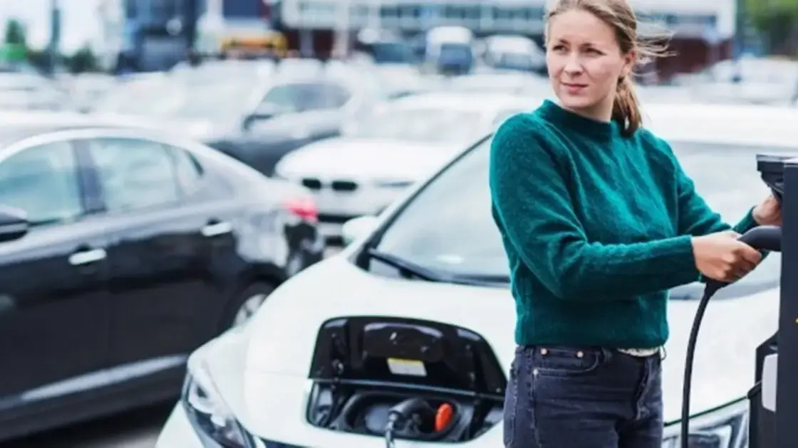 Woman in a green sweater charging a white car in the street