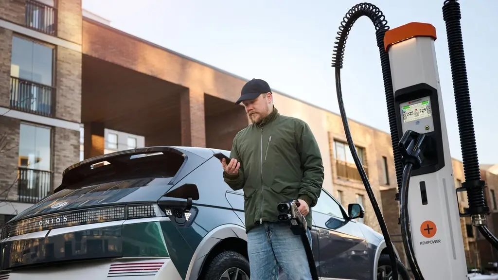 man with spring jacket and cap charging car in front of habitation building