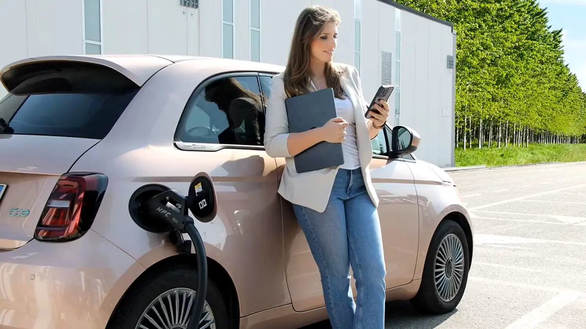 Donna davanti a un'auto rosa con computer e smartphone in mano