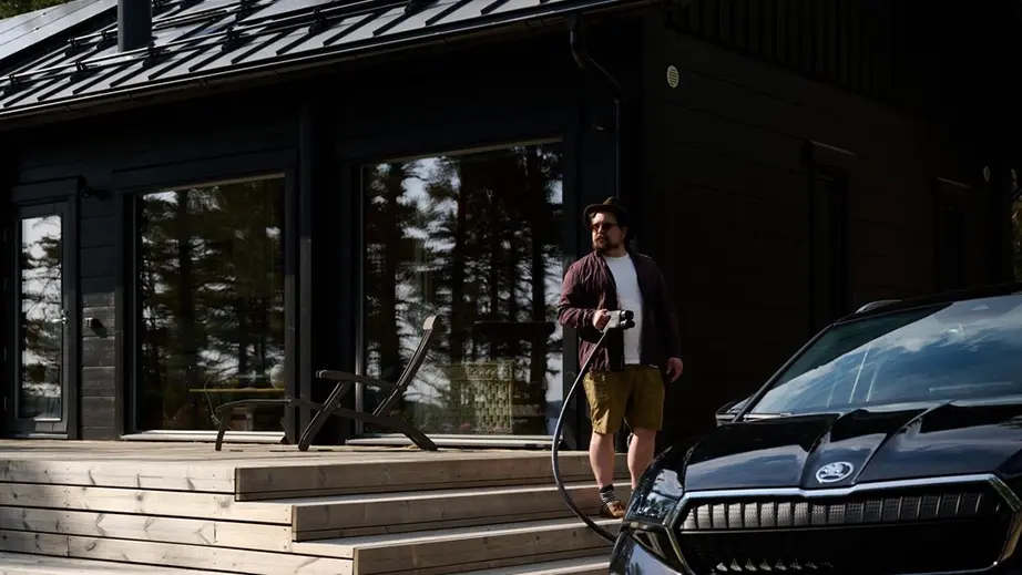 Homme qui recharge son véhicule devant une maison dans les bois 